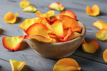 Bowl with rose petals on wooden background