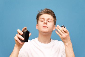 Close up portrait of a boy in a white T-shirt stands on a blue background, spray perfume and smells...