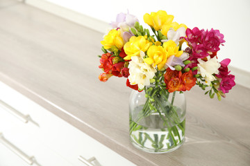 Beautiful bright spring freesia flowers in vase on chest of drawers. Space for text
