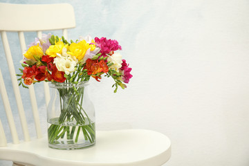 Beautiful spring freesia flowers in vase on chair. Space for text