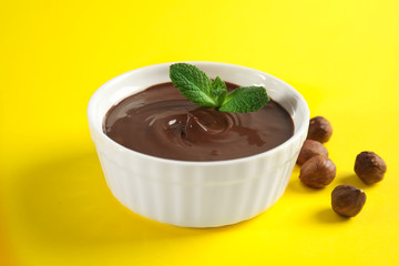Ceramic bowl with sweet chocolate cream, hazelnuts and mint on color background