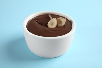 Ceramic bowl with sweet chocolate cream and hazelnuts on color background