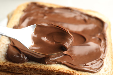 Spreading sweet chocolate cream onto toast with spoon, closeup