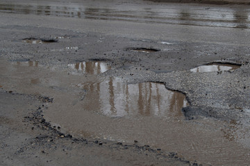 Water filled potholes on a rough road.Several potholes. Bits of gravel on road. Puddles (potholes) on the road, rainy weather.