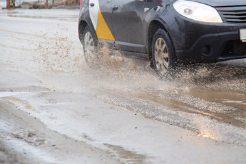 Moving car sprays puddle when heavy rain drops on concrete.