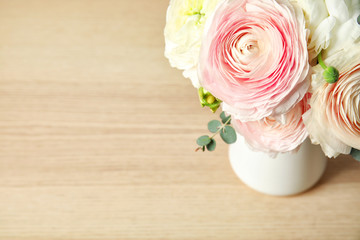 Beautiful spring ranunculus flowers in vase on wooden table. Space for text