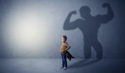 Little waggish boy in an empty room with musclemen shadow behind
