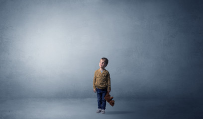 Little waggish kid staying alone in a big empty room with his plush
