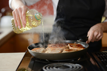 The chef in the kitchen prepares fresh pork steaks on a griddle with steam, the menu is homemade cooking culinary recipes. restaurant menu. Delicious food, recipes and cooking