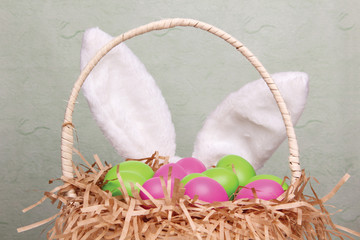 Rabbit's ears behind a wicker basket full of colorful Easter eggs