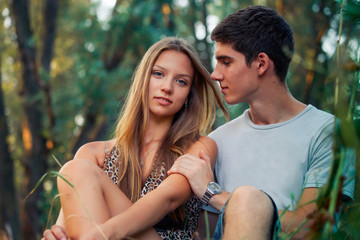 Obraz premium Guy and girl are sitting by water in summer. In love couple are looking to each other. Beautiful couple in water. Children on vacation are resting in nature.