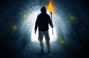 Ugly man with burning flambeau walking in a dark tunnel