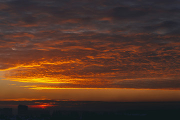 Cityscape with vivid fiery dawn. Amazing warm dramatic cloudy sky above dark silhouettes of city...