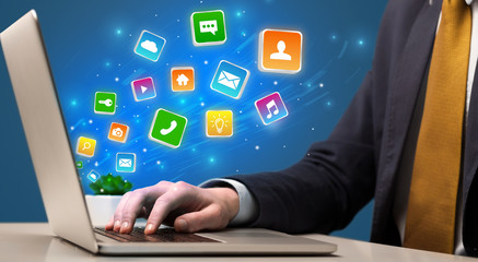 Businessman hand typing on laptop with flying application icons around
