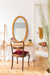 Stylish and elegant home interior with wooden desk, retro chair, design accessories, gold lamp and dressing table with mirror. Piece of design woman's room. Open space. Minimalistic and warm space.