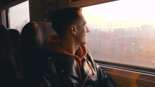 Young man having train journey. Man looking out the window during train ride at sunset