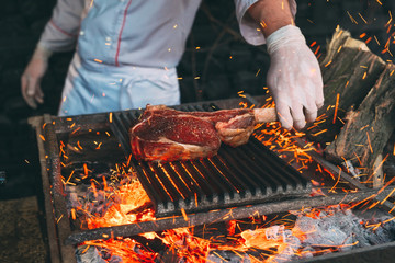 Chef Cooking steak. Cook turns the meat on the fire. - obrazy, fototapety, plakaty
