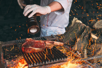 Chef pepper the steak on fire. - obrazy, fototapety, plakaty