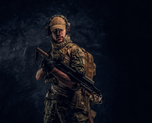 Fototapeta na wymiar Fully equipped soldier in camouflage uniform holding an assault rifle. Studio photo against a dark wall