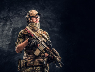 Fully equipped soldier in camouflage uniform holding an assault rifle. Studio photo against a dark...