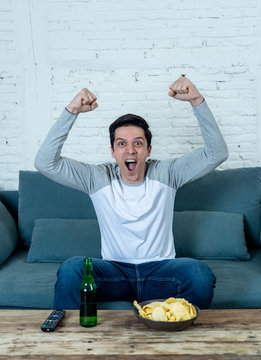 Excited Young Man Sitting On The Couch Watching Football. Sports Supporters And Fans Concept