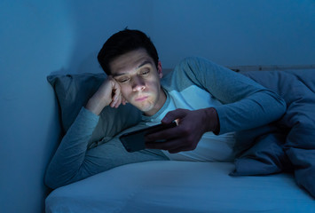 Young caucasian sleepless man bored in bed surfing on the Internet addicted to mobile phone