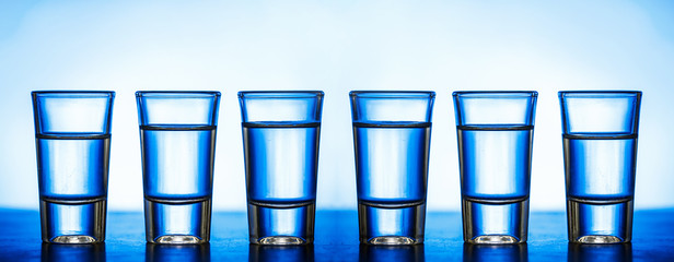 Glass vodka shots in a row. Weekend party blue alcohol background.
