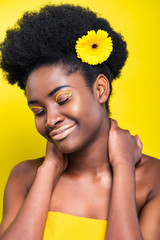 Smiling beautiful african american woman with flower isolated on yellow