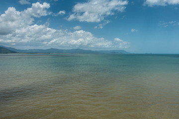 Cairns, Australia - February 17, 2019: Shallow and calm Coral Sea water in front of the town. Horizon of mountains north of the city part of Kuranda National Park under blue sky with white cloudscape.