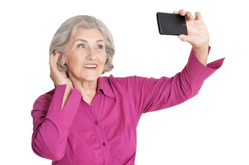 Beautiful senior woman taking selfie with smartphone on white background