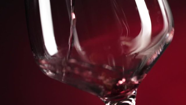 Wein. Rotwein, der in Weinglas &uuml;ber dunklem Hintergrund gie&szlig;t.