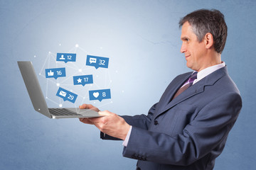 Man holding laptop with different types of social media symbols and icons
