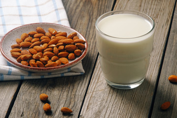 Glass of almond milk with almond nuts on rustic wooden table. Vegan alternative food, non-dairy milk, clean eating concept.