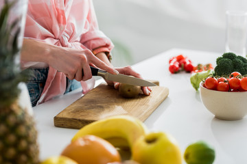 cropped view of woman cutting kiwi fruit near ingredients in kitchen