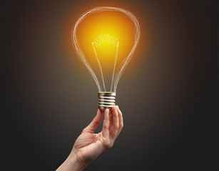 Hand holding light bulb on dark background. New idea concept