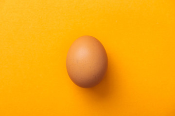 top view of whole brown chicken egg on bright orange background