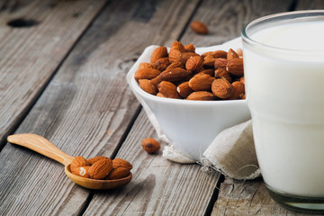 Homemade almond milk in glass, bowl and spoon with almonds on rustic wooden table, close up.