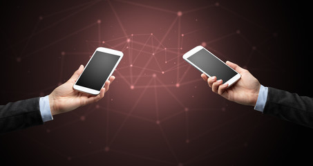 Close up of two hands holding smartphones to each other, wireless connection concept