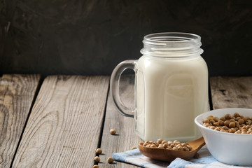 Healthy organic soy milk dairy free alternative in jar and bowl with soybean on dark wooden background. Vegan milk lactose free concept.