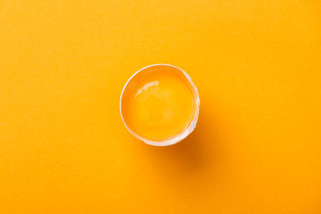 top view of smashed chicken egg with yolk on bright orange background