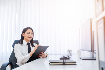 Fototapeta premium Attractive businesswoman writing information on her clipping board while sitting in her modern office.