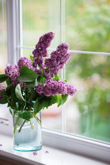 Spring tender bouquet of beautiful lilac in glass vase near window in daylight
