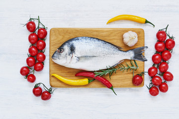 Raw dorada fish with vegetables on wooden cutting board. Healthy food concept. Top view, copy space.
