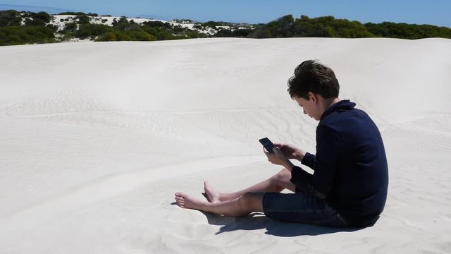 Recieving a message in remote place, boy alone on the desert sand dune