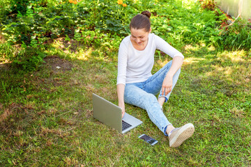Freelance business concept. Young woman sitting on green grass lawn in city park working on laptop pc computer. Lifestyle authentic candid student girl studying outdoors. Mobile Office