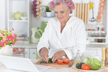 Portrait of senior woman in hair rollers cutting vegetables on kitchen table