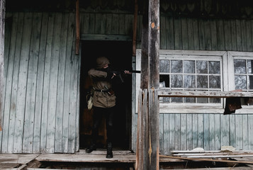 Stalker, a soldier in uniform and with a gun is standing on the porch of an old, abandoned house