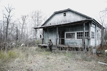 Stalker, a soldier in uniform and with a gun is standing on the porch of an old, abandoned house