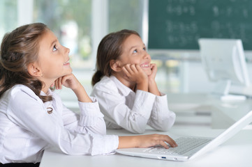 Portrait of two beautiful little girls at class with laptop