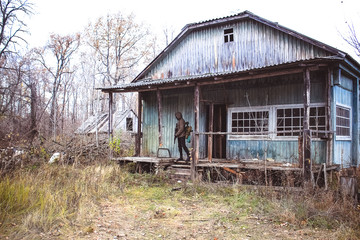 Stalker, a soldier in uniform and with a gun is standing on the porch of an old, abandoned house